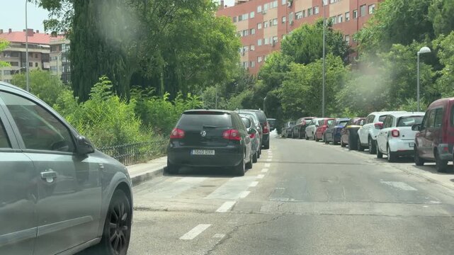 Madrid, Spain, June 25, 2026: Editorial driving footage along broad residential streets with parked vehicles, tree-lined avenues and apartment buildings before approaching a pedestrian crossing during