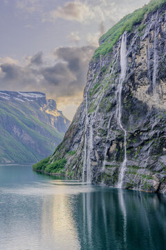 Geiranger, Majestic Norwegian Fjord Landscape, Dramatic fjord landscape with steep, green mountains and calm water under a cloudy sky. Serene natural beauty.