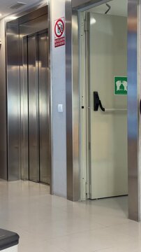 Static shot of a modern elevator lobby with stainless steel elevator doors and one open doorway inside a contemporary public building.