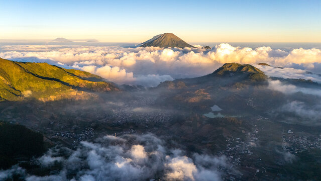 Aerial view of the volcanic landscape of the Dieng Plateau with mountain peaks rising above a sea of clouds at sunrise, Indonesia.