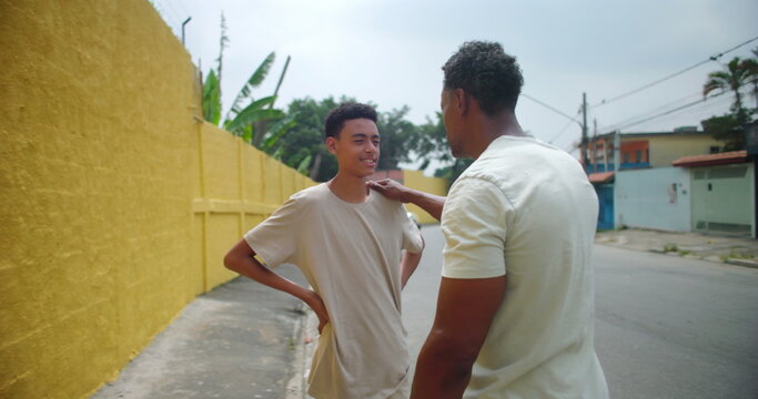 Father of African descent talking to son in an urban street, offering advice and encouragement with a reassuring gesture, emphasizing connection, mentoring, and family bond