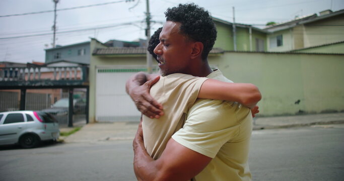 Father of African descent holding son in a strong embrace in an urban street, expressing unconditional love, emotional support, and the strength of their family bond