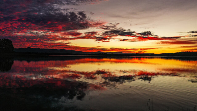 Aerial view of Lake Samsonvale at sunset with vibrant red and orange clouds reflecting on the calm water surface in City of Moreton Bay, Queensland, Australia.