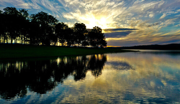 Aerial view of Lake Samsonvale at sunset with silhouetted trees reflecting on the calm water surface in City of Moreton Bay, Queensland, Australia.