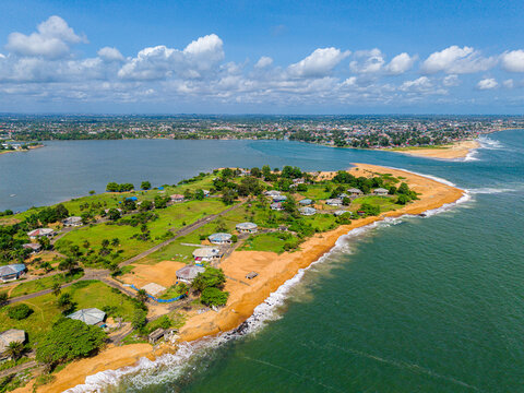 Aerial view of residential houses along the sandy coastline, lush green vegetation, and the meeting point of the lagoon and the Atlantic Ocean, Monrovia, Montserrado, Liberia.