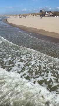Waves roll onto wide sandy beach along North Sea coast with visitors walking on shoreline in Belgian seaside resort. Beach recreation, seaside landscape, waterfront destination