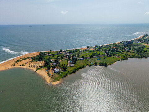 Aerial view of a coastal peninsula with scattered buildings, lush greenery, and sandy beaches situated between the Atlantic Ocean and a calm lagoon in Monrovia, Montserrado, Liberia.