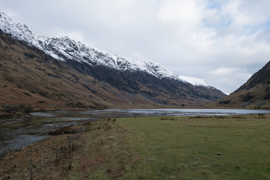 Looking east over the River Coe, Loch Achtriochtan and the A82 road to the snow capped Aonach Eagach Ridge, Glencoe, Scottish Highlands.