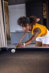 Naklejka premium Woman lining shot, leaning over dark felt pool table at home, aiming cue and bridge hand