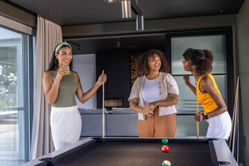 Obraz premium Diverse female friends standing around black felt pool table in modern game room holding cues
