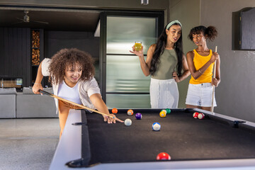 Naklejka premium Diverse female friends playing pool in game room by black felt table with cues and balls
