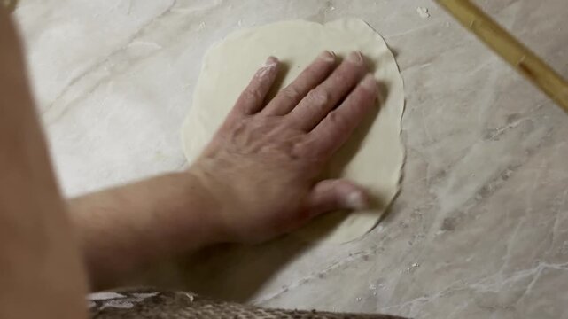 Close up of hands rolling out and smoothing raw dough with a thin wooden pin on counter