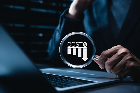 Cost reduction and business expense optimization concept. Businessman holding magnifying glass looking at declining bar chart icon with dollar sign, budget cutting and corporate profit analysis.