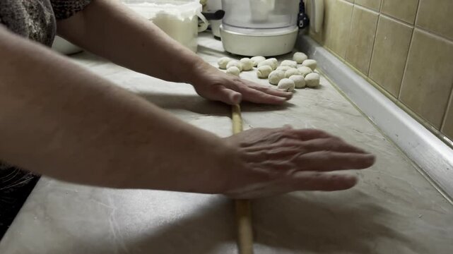 Cook flattening dough with wooden rolling pin on kitchen counter top