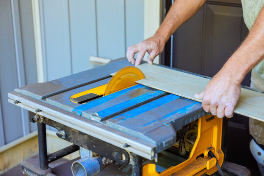 Contractor operated table saw to cut piece of wood while standing outside by house