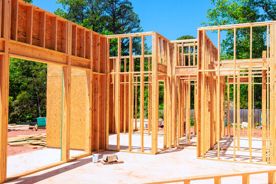 Construction continues with wooden beams frames wall being built in an outdoor setting with unfinished house