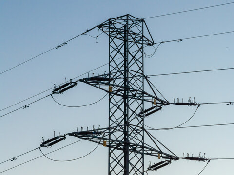 Aerial view of a high-voltage electricity pylon with power lines against a clear blue sky in Warsaw, Masovian Voivodeship, Poland.