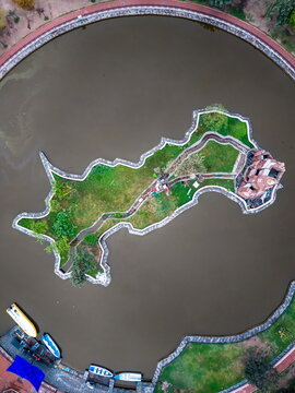Aerial view of the map-shaped island in a lake with a small building, lush green grass, and surrounding water in Lahore, Punjab, Pakistan.