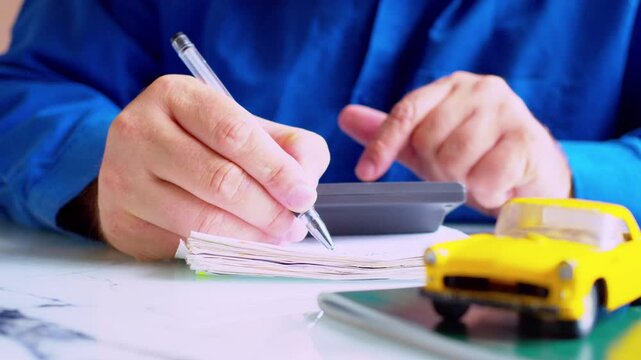 Insurance specialist calculating compensation and filling claims form at desk. Close up on hands, yellow toy car on table, shallow depth of field, natural daylight. 