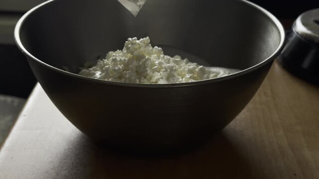 Adding white cottage cheese curd into a metal bowl with albumin mixture