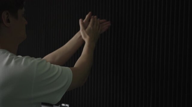 Young sound engineer clapping hands to test acoustic absorption of new soundproofing foam panels, evaluating the room echo and reverberation for audio quality improvement, close-up, slow motion.