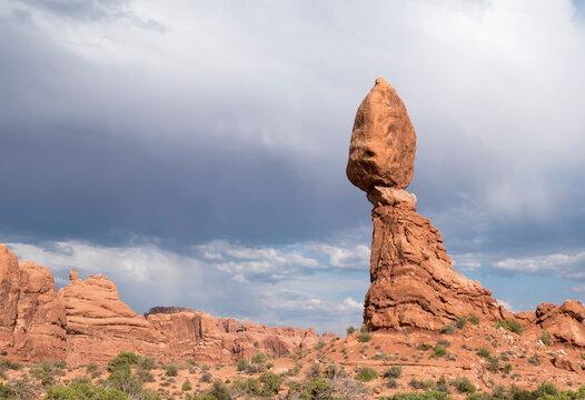 Balanced Rock in Arches National Park with dark stormy clouds rolling in, daytime. Famous landmark inside Arches National Park in Moab, Utah, USA.