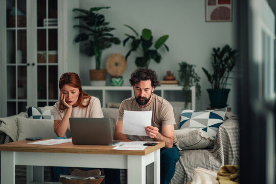 Financial stress impacting a couple paying bills at home, managing debt and expenses on a laptop in the living room
