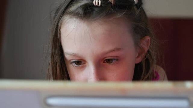Young girl concentrates on tablet screen at home while watching digital content or completing an online learning activity.