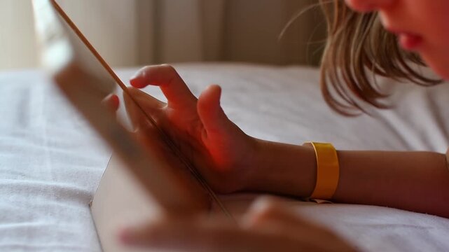 Child uses touchscreen tablet on hotel bed during quiet indoor leisure, family travel rest and digital screen entertainment.