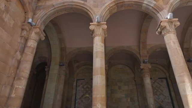 Walk through the beautiful stone colonnade of the historic Jermuk Mineral Water Gallery in Armenia, showcasing classical architecture with elegant arches and columns on a bright sunny day.

