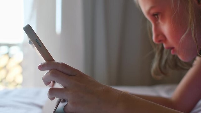 Girl plays mobile game on tablet in bed instead of outdoor walk; screen time replaces exercise and active childhood leisure.