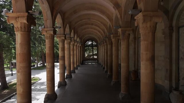 Walk through the beautiful stone colonnade of the historic Jermuk Mineral Water Gallery in Armenia, showcasing classical architecture with elegant arches and columns on a bright sunny day.

