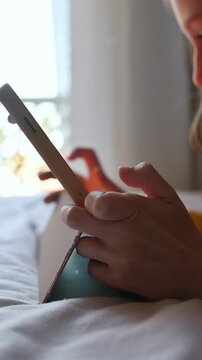 Close up of child actively playing game on tablet in bed at home, tapping screen during indoor rest and digital leisure time