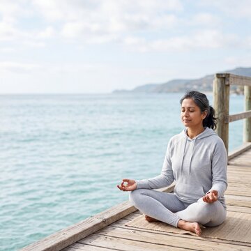 Serene middle-aged woman practicing meditation and mindfulness on a wooden pier by the ocean