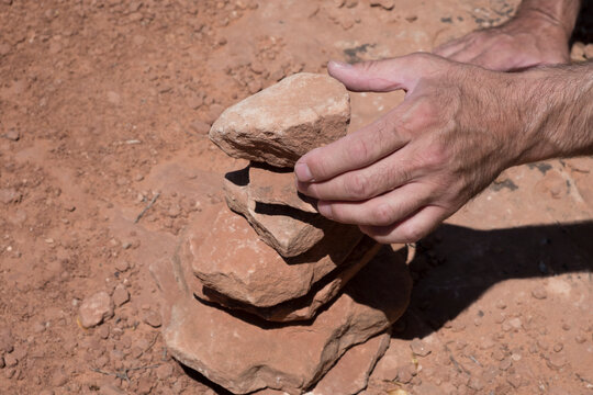 Caucasian man stacking rocks on the side of the trail in the desert to create a cairn. Trail marker in the desert of Utah, arid wilderness. Marking trail with rocks as to not get lost. Daytime.