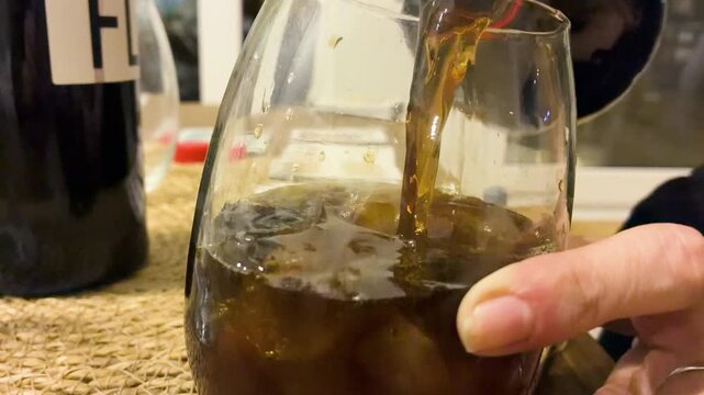 Close up of pouring dark cola into glass with ice and fernet to prepare traditional Argentine cocktail