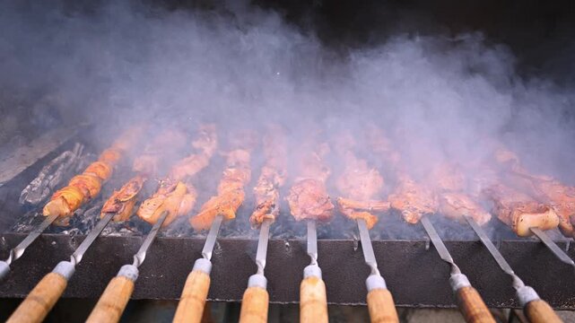 Rows of skewers cook over hot coals, smoke rising. Meat pieces sizzle, charred slightly on edges. Wooden handles grip each skewer firmly. Grill emits thick smoke, creating warm, smoky atmosphere