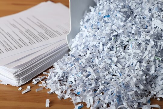 Shredder with cut paper pieces and documents on wooden table, closeup
