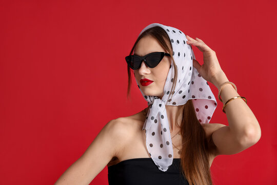 Beautiful woman in stylish sunglasses and headscarf on red background, space for text