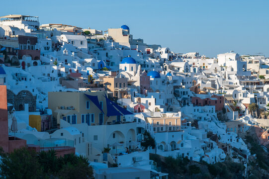 Scenic view of Oia&rsquo;s white and blue architecture cascading down the cliff on Santorini island, Greece, in warm evening light.