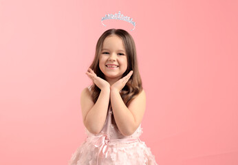 Cute little girl with crown above her head dreaming to be queen. Pink background