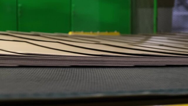Detail shot of stacked and overlapping brown cardboard layers moving continuously on an industrial conveyor belt line.