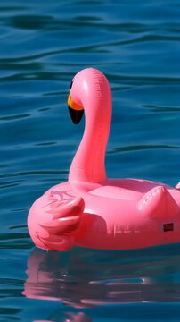 A pink inflatable flamingo floatie partially submerged in calm, deep blue water
