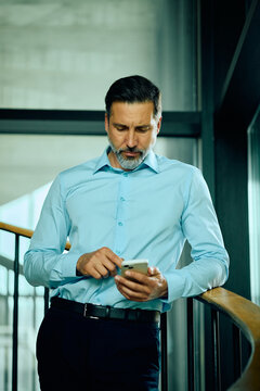 Middle aged businessman checking smart phone messages while working in the office.