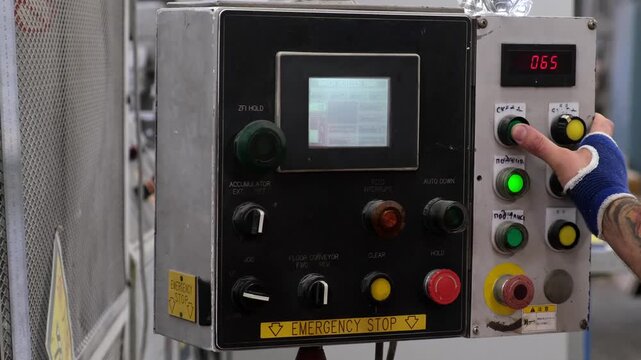 Close up of a worker hand pressing a green button on a mechanical control console with an emergency stop button.