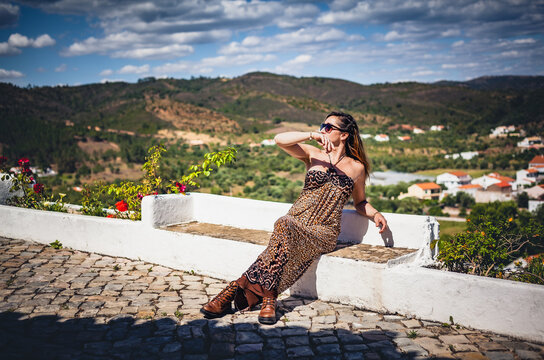 Woman in maxi dress sitting on white wall viewpoint overlooking Salir countryside