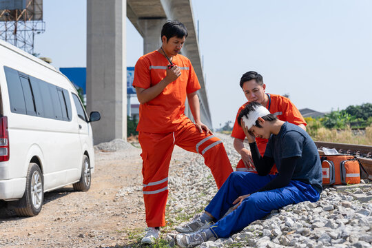 emergency rescue providing first aid help to injured worker with head bandage at railway,asian man paramedic using walkie-talkie to coordinate medical team for referral to a hospital