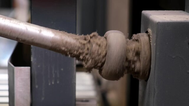Macro shot of a spinning machine shaft accumulating recycled paper dust and fiber debris in an automated cardboard factory.