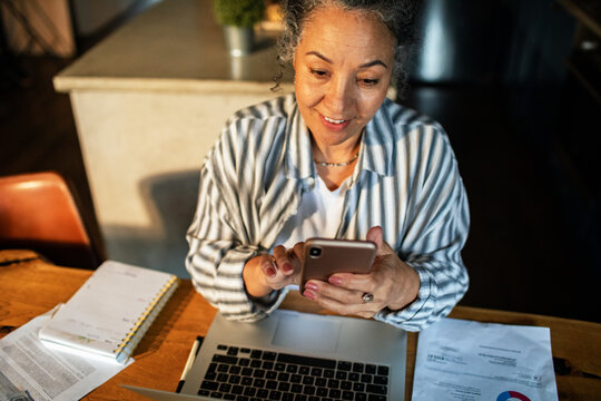Senior woman managing finances on smartphone at home desk