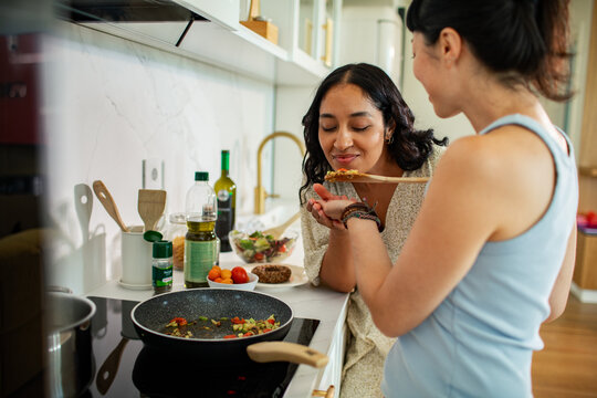 Two women cooking and tasting food in a home kitchen
